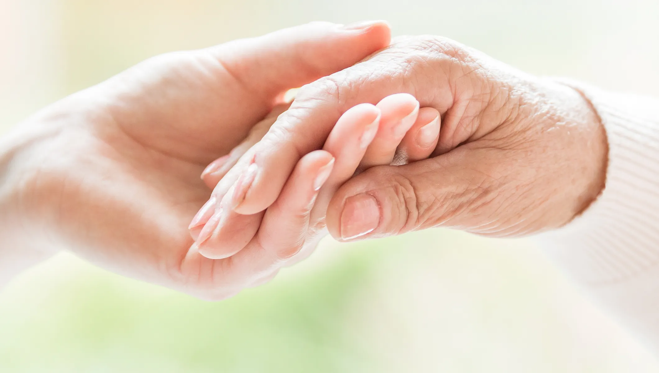 Eine ältere Hand wird einfühlsam von einer Pflegehand gehalten und vermittelt Nähe, Vertrauen und menschliche Zuwendung