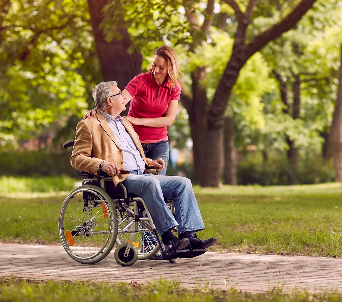 Pflegekraft begleitet einen Senior im Rollstuhl bei einem Spaziergang im Park und sorgt für Mobilität und persönliche Betreuung