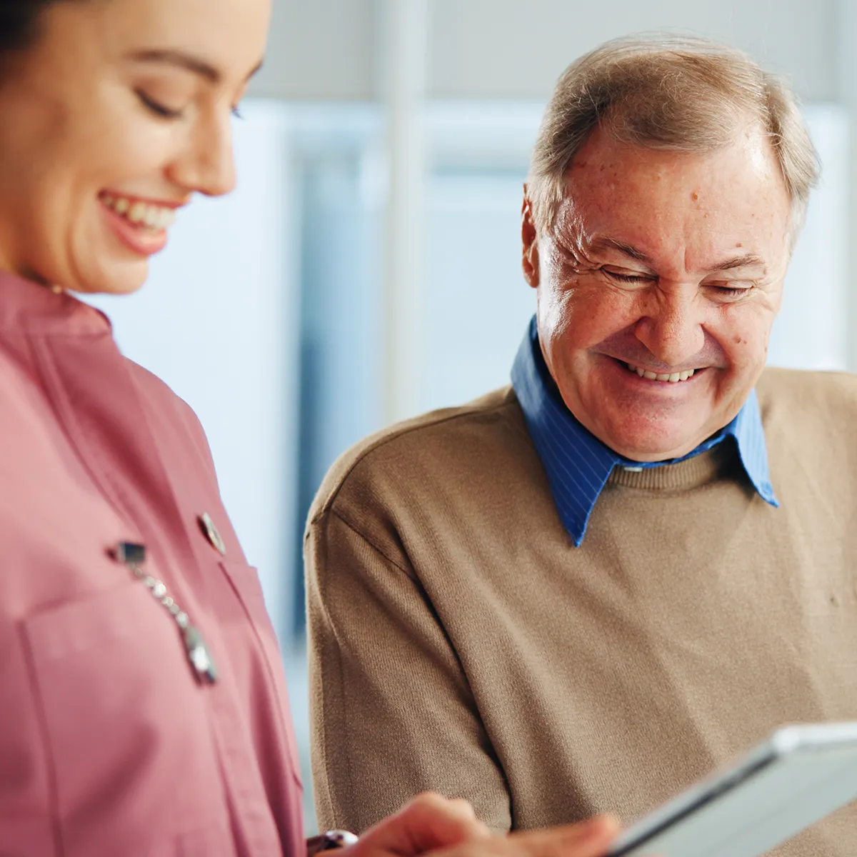 Pflegekraft unterstützt einen Senior bei der Nutzung eines Tablets und fördert Selbstständigkeit im häuslichen Umfeld