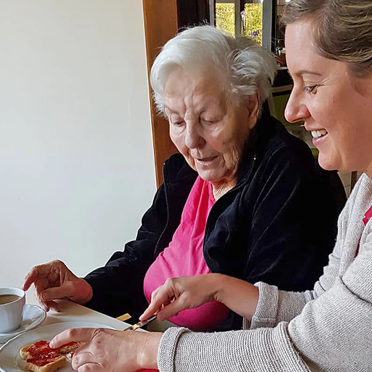 Seniorin bereitet gemeinsam mit einer Betreuungsperson ein Frühstück zu und wird im Alltag einfühlsam unterstützt