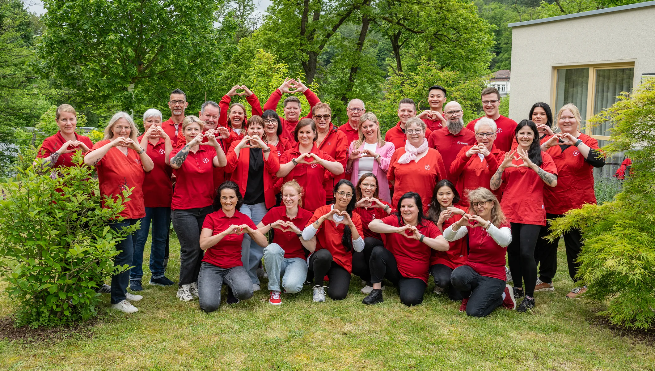 Herzwohl Team bei einem Gruppenfoto im Garten mit Herz-Geste als Zeichen für Pflege mit Herz